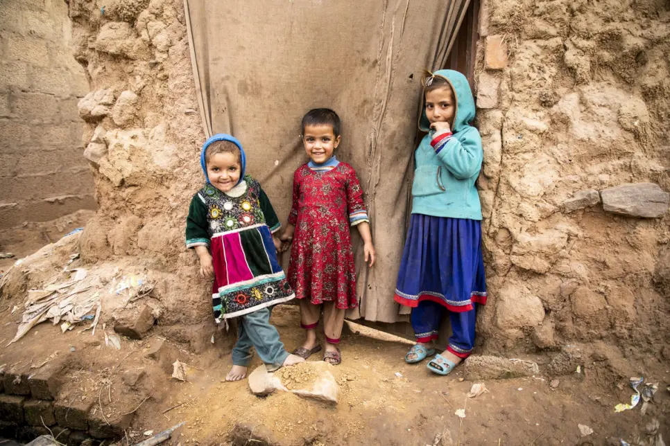 Three Afghan children stand outside of a doorway 