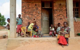 A group of people sit outside of a building in the DRC