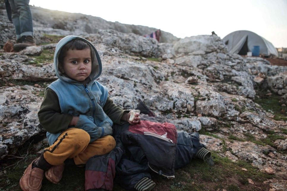 A child from Idlib sits on a rock by a tent