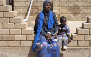 A woman from Niger sits on a partially built brick wall