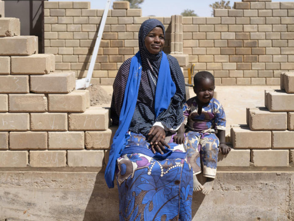 A woman from Niger sits on a partially built brick wall