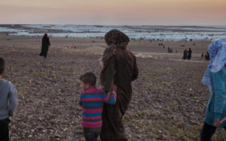 A mother from Syria walks on a beach with her children