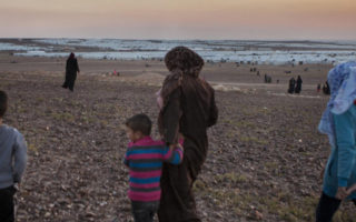 A mother from Syria walks on the outskirts of a refugee settlement with her children