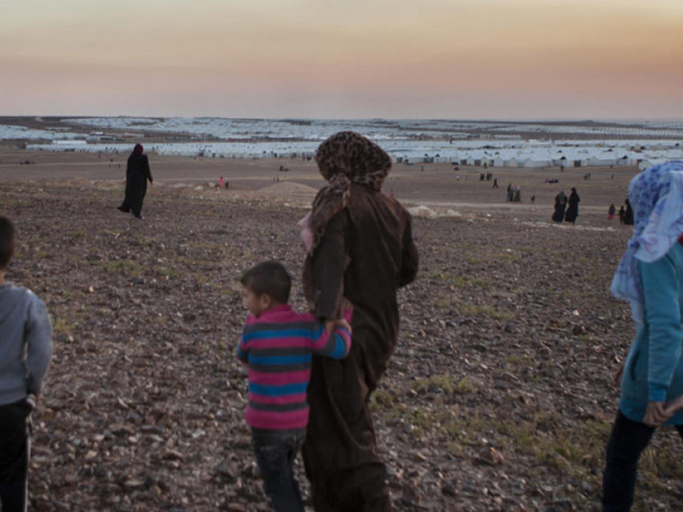 A mother from Syria walks on the outskirts of a refugee settlement with her children