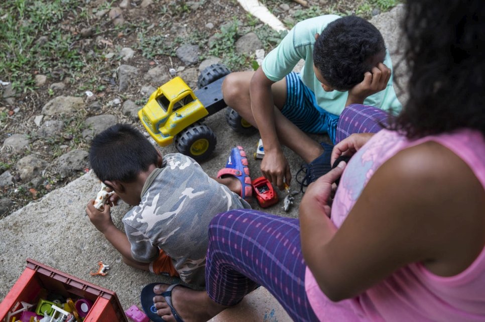 Woman sits on a bench watching her two sons play with toys on the ground in Nicaragua