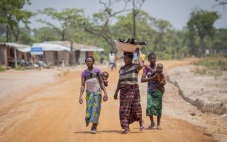 Three women walking carrying a basket and children in the DRC