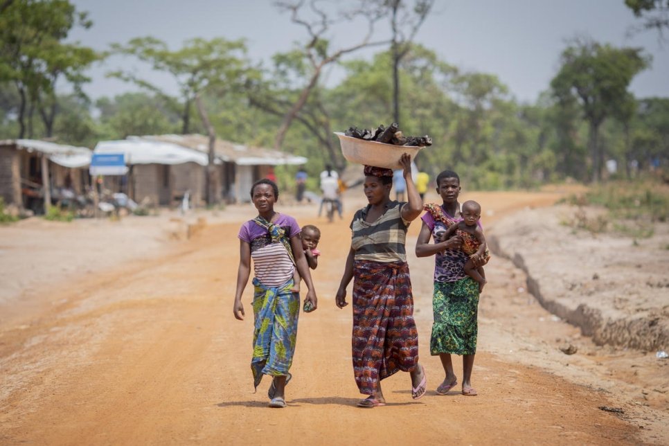 Three women walking carrying a basket and children in the DRC