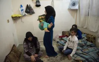 Woman carrying her child with her family sitting on the floor around her in Syria