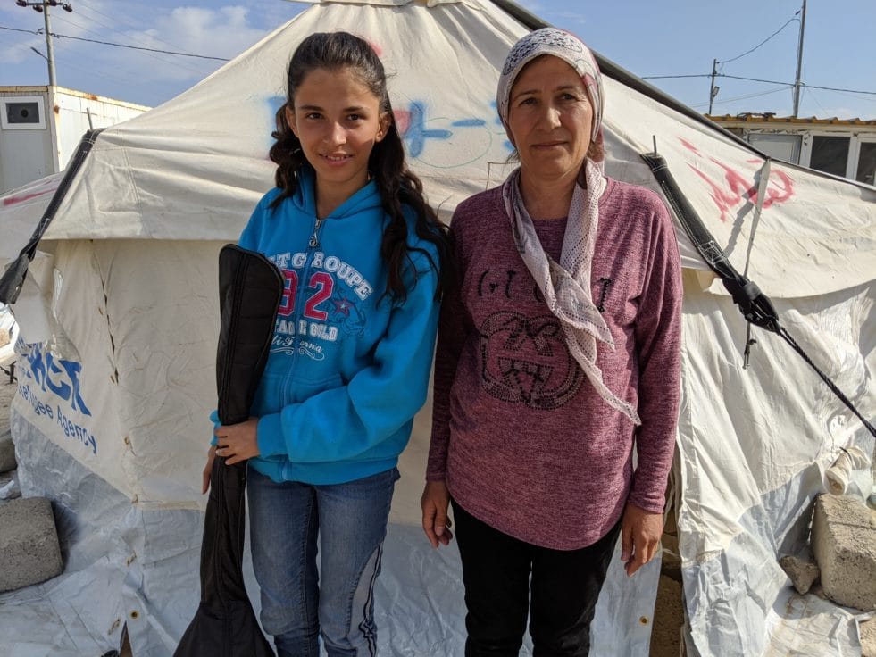 A girl from Syria and her mother standing in front of a tent