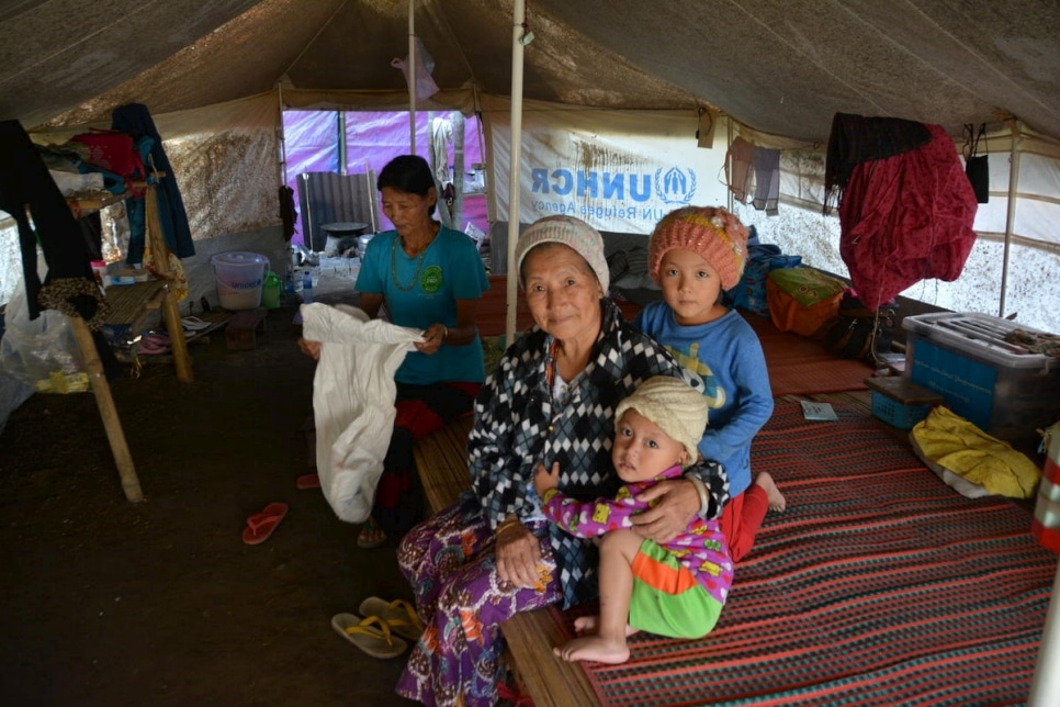 Two women and two children sit close to each other in a tent with the UNHCR logo visible in the background