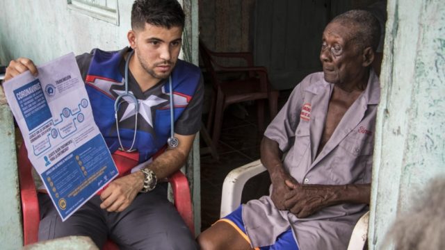 A young man with a stethoscope around his neck explains a poster to an older man