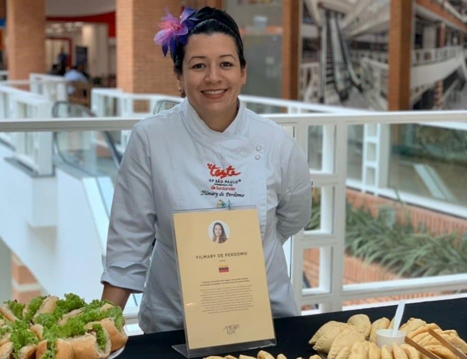 A woman in a chef's smock poses behind her food stall