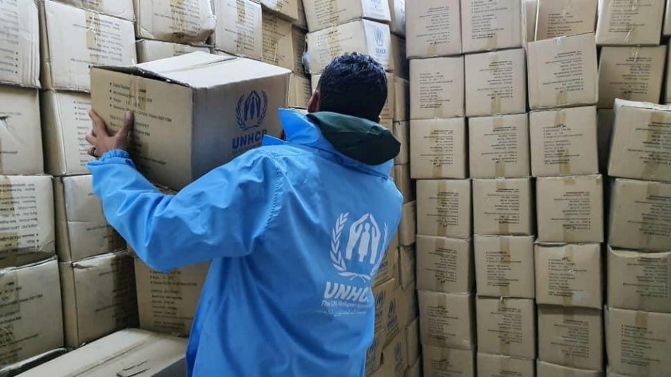 A man wearing a UNHCR jacket stacks boxes of relief supplies in Libya