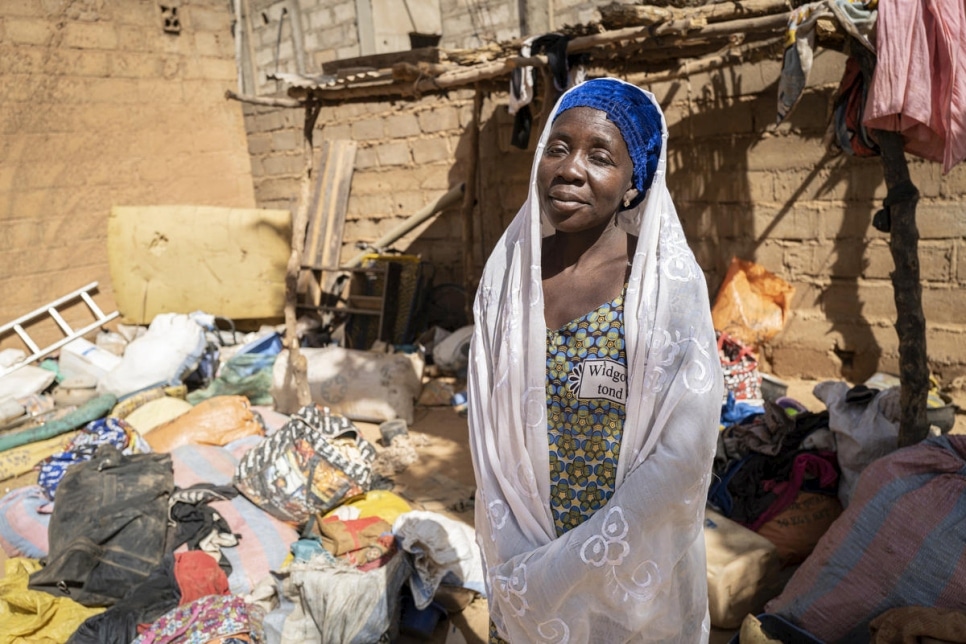 Woman stands in front of a shack with clutter surrounding her in Burkina Faso
