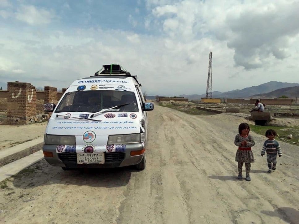 White vehicle on dirt road with children walking beside it in Afghanistan