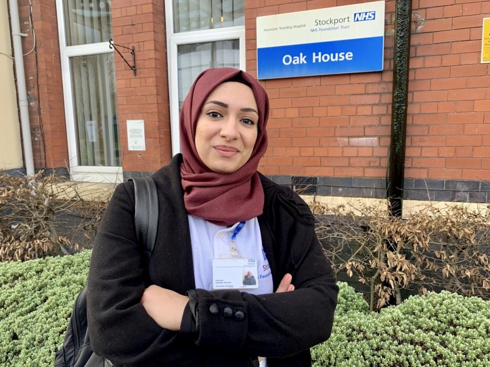 A woman with a hijab stands in front of the outside of a hospital