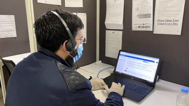 A man working at a call centre with a headset on in front of a laptop