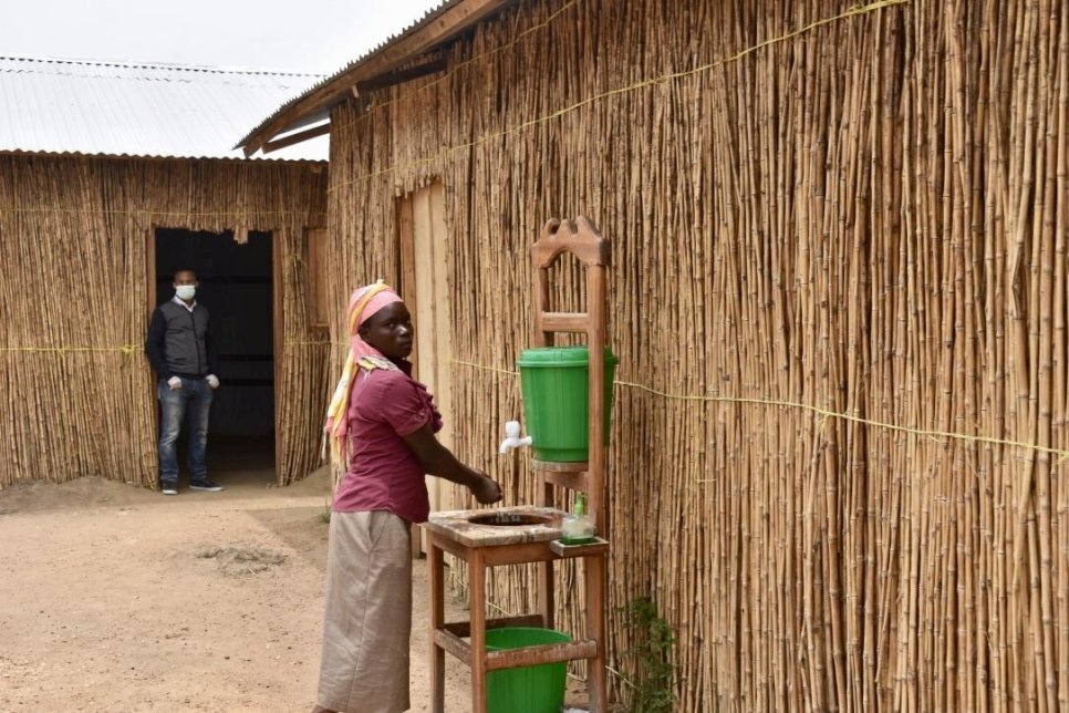 A woman washes her hands at a washing station outside of a straw building in the DRC