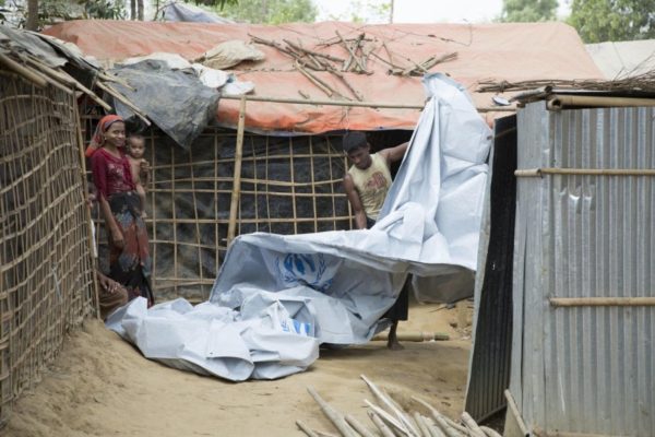 A man unravels a large white tarp while a woman carrying a child looks on