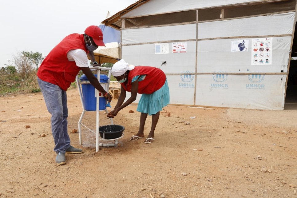 A man helps a woman wash her hands at a designated washing station