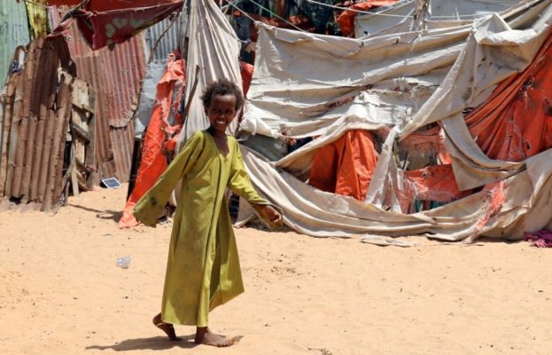 A young girl walks barefoot in front of some makeshift tents