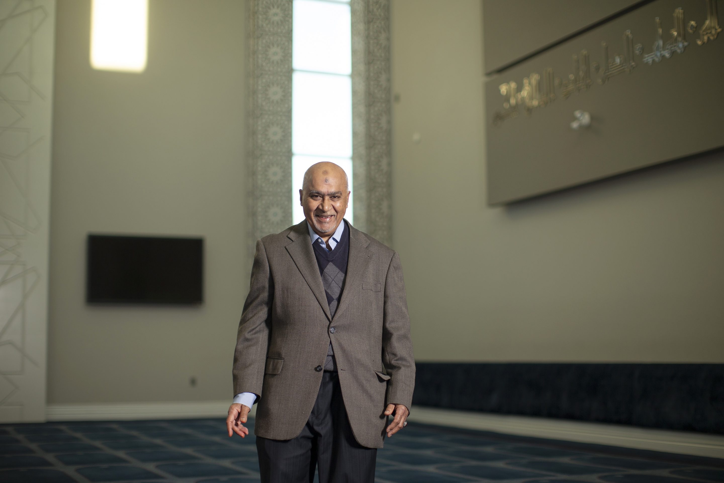 A man in a suit stands in a hall in front of a window