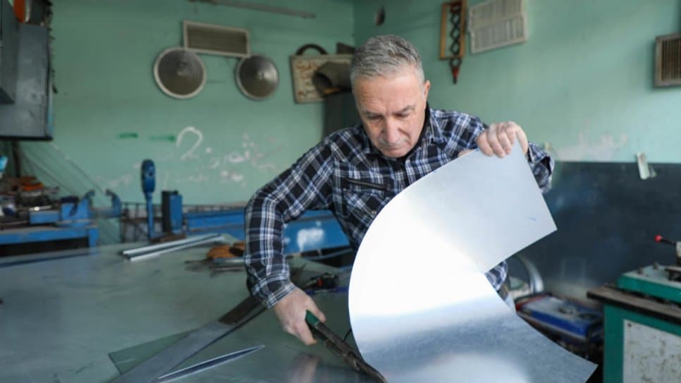 Mosul resident Saad cuts sheet metal to make wood-burning stoves for his returning neighbours
