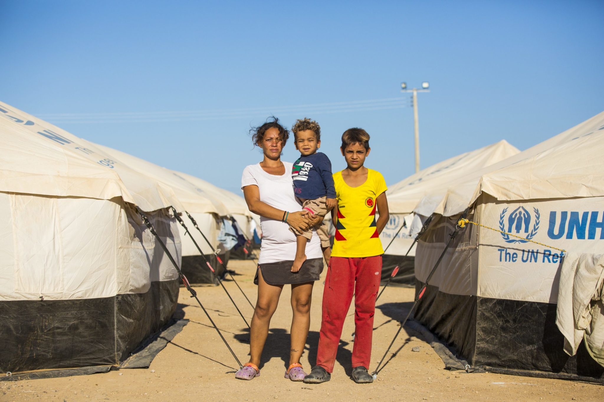 A mother with her two children stand between two rows of tents