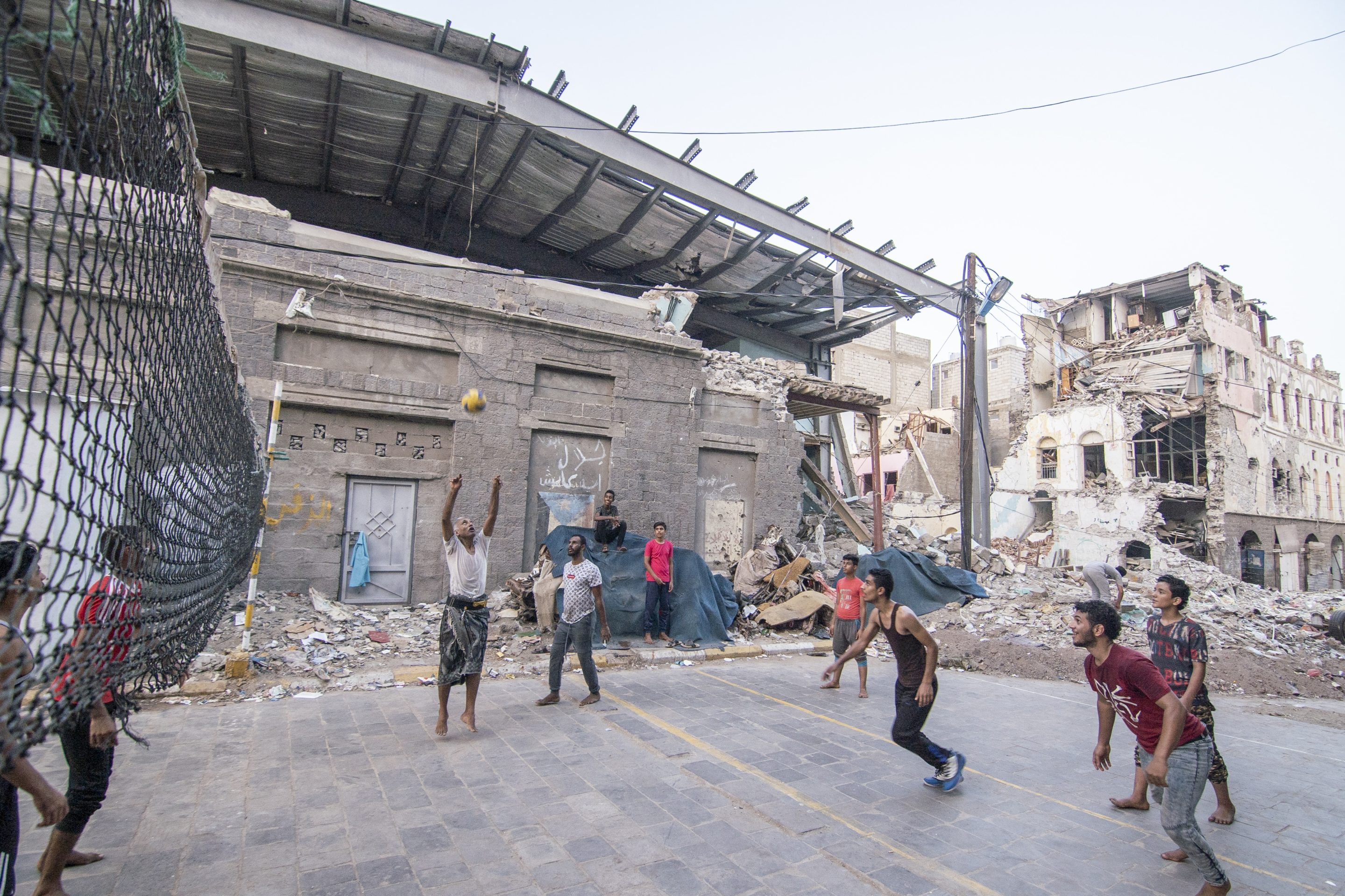 A group of people play volleyball among war ruins