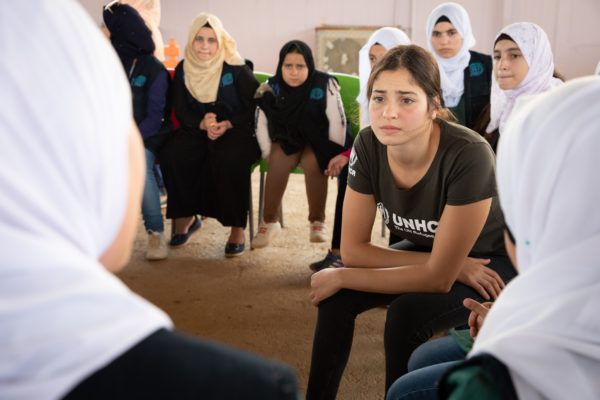 A woman hunches over her knees to listen to two other women