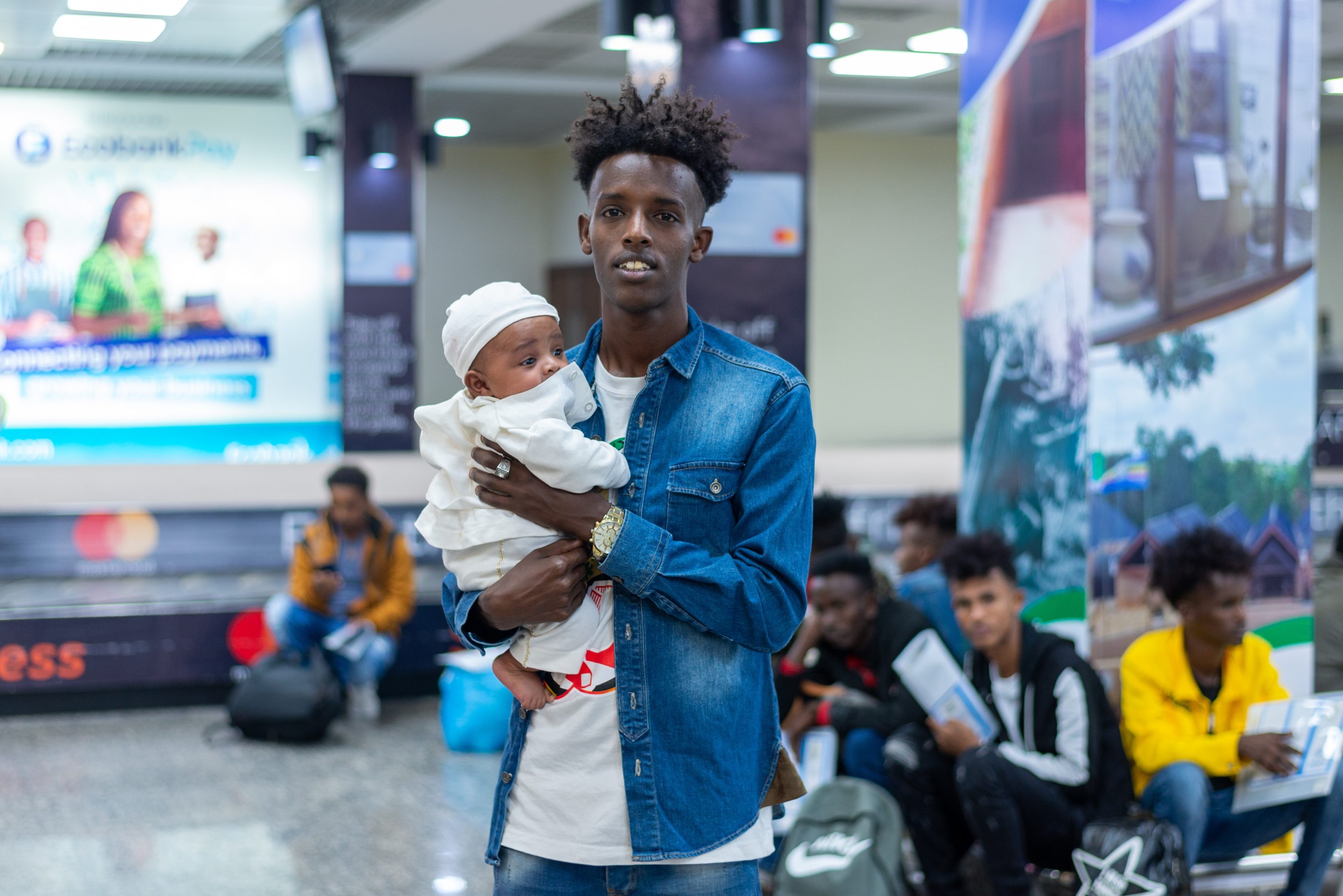 A man stands in an airport lobby carrying his child
