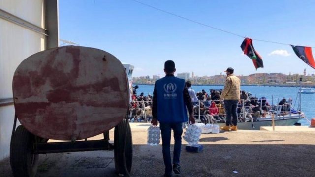 UNHCR staff distribute bottled water to refugees and migrants whose vessel was intercepted attempting to cross the Mediterranean Sea and returned to Libya on April 9