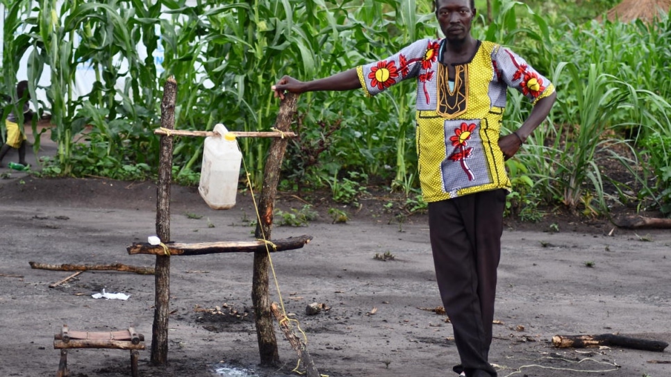 Chris, un réfugié sud-soudanais, se tient à côté du point d'eau avec un robinet à bascule qu'il a fabriqué dans son enclos situé dans le site de Bele, en République démocratique du Congo