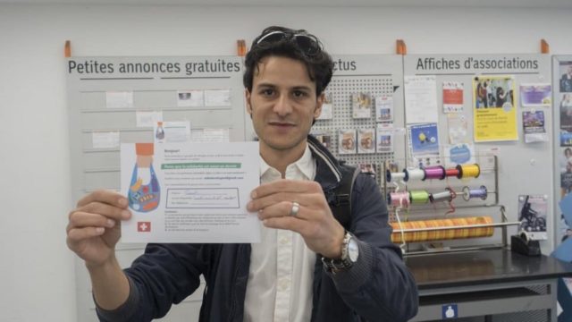 Shadi Shhadeh holds up a flyer offering the support of Syrian refugees to shop for COVID-19 most vulnerable in Geneva and Lausanne, Switzerland