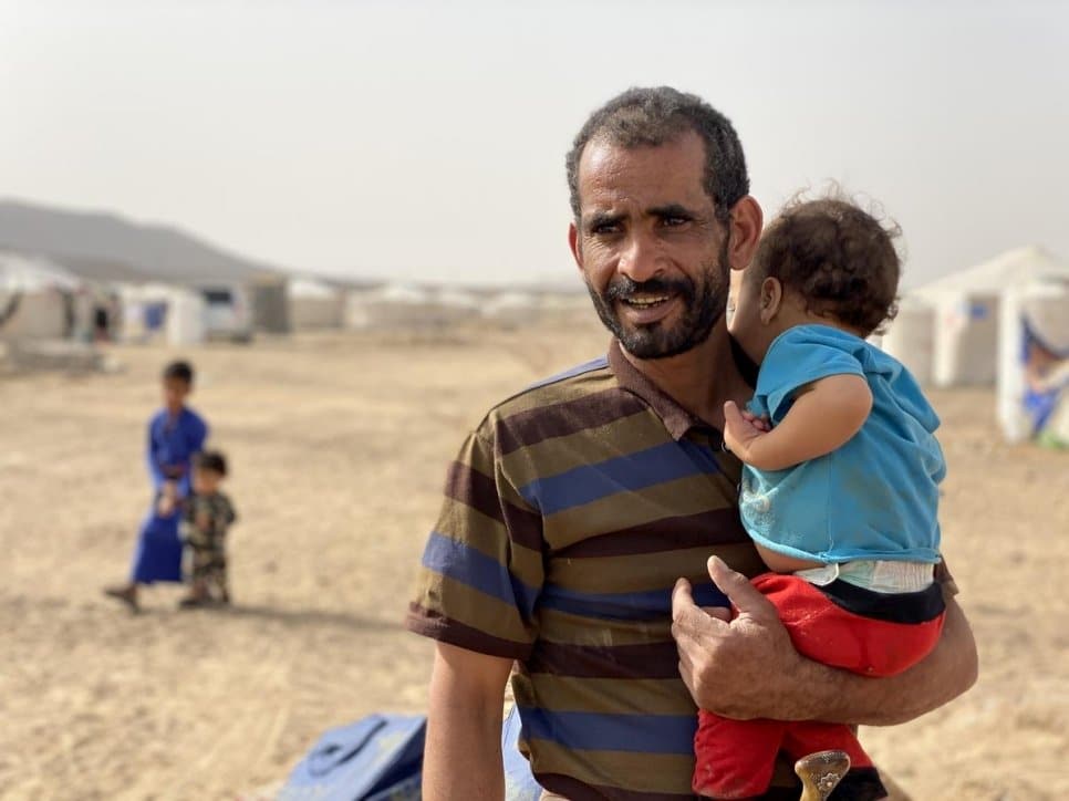 Taher, un Yéménite de 40 ans et déplacé par le conflit, tient dans les bras son plus jeune fils Mustafa, 2 ans, devant leur abri dans le site d’accueil des personnes déplacées au camp de Marib