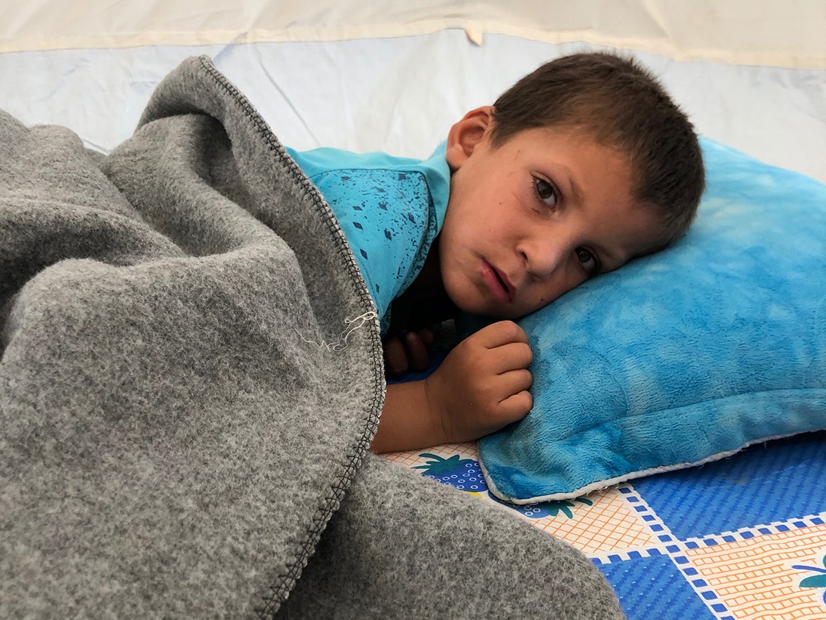A Syrian boy lays on a bed under a blanket