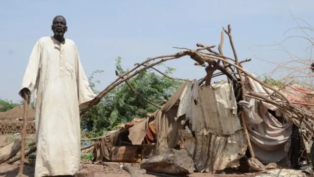 South Sudanese refugee, Bak, 80, stands next to his shelter that was damaged by massive flooding in Sharq Al-Nile, Sudan.