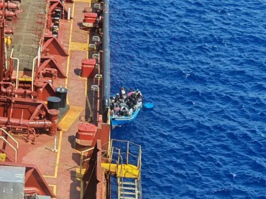 Migrants and refugees sit in a boat alongside the Maersk Etienne tanker off the coast of Malta, in this handout image provided 19 August, 2020