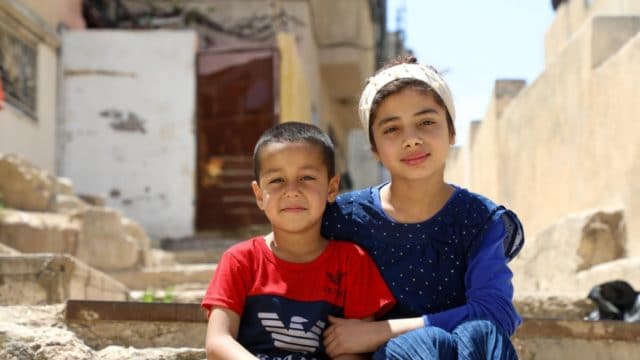 Nadia, 12 ans, et son plus jeune frère Abed, 5 ans, sont assis dans la ruelle devant leur maison à Amman-Est. Avec leurs trois autres frères et soeurs, ils utilisent à tour de rôle la seule télévision et le seul téléphone portable de la famille
