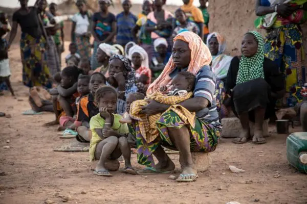 Women and children sit outside a house