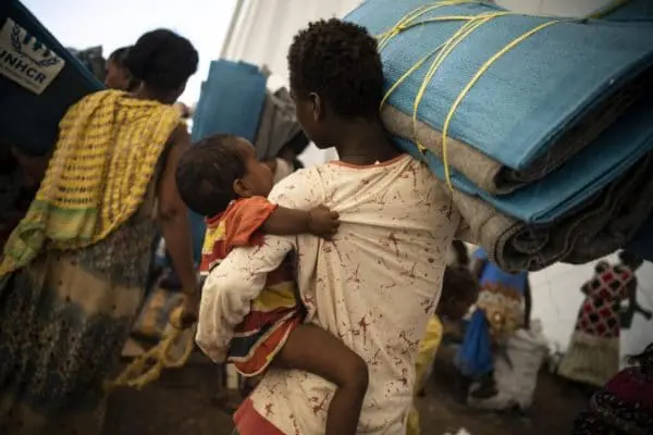 Une réfugiée éthiopienne et son enfant reçoivent des nattes de couchage dans un site de transit à Hamdayet, au Soudan.