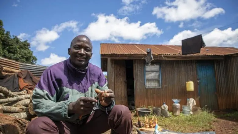 Refugee and artisan Kapya Kitungwa smiles in front of a home.