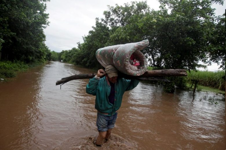 A man carries his belongings through a flooded road.