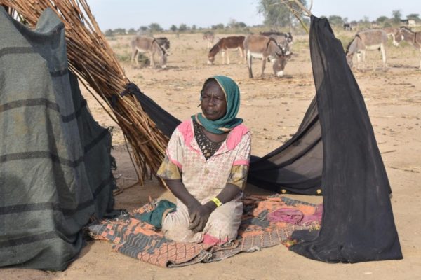 Woman kneels in front of a makeshift shelter.