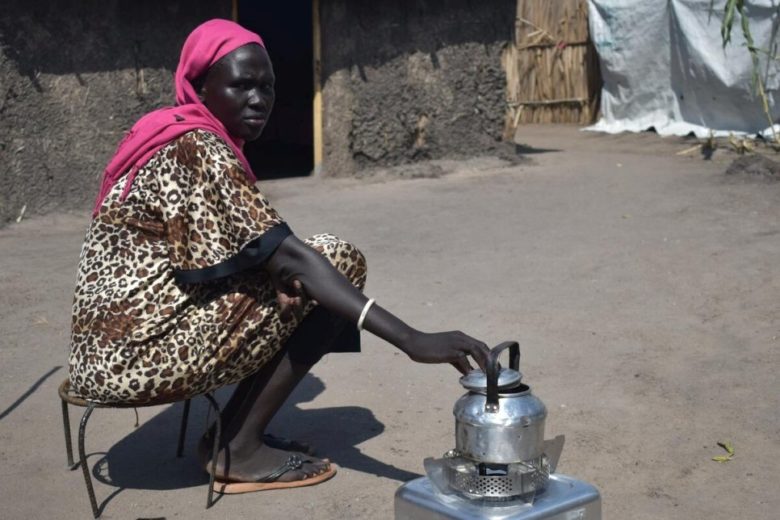 Woman warms kettle atop an ethanol stove.