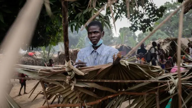 Un homme construit un toit avec des feuilles de palmier.