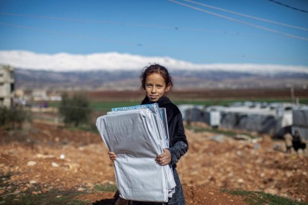 A young Syrian refugee carries plastic sheeting for her family’s shelter in Lebanon’s Bekaa Valley