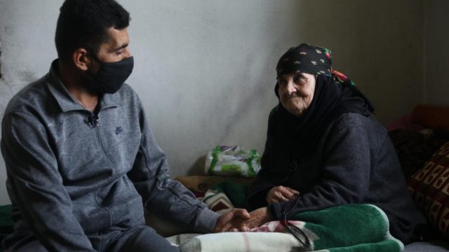 Amina, 85 ans, est assise sur son lit avec son fils Abdo dans la maison qu’ils partagent à Touline, au Liban.