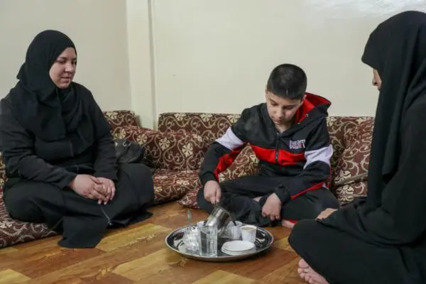 Ali, 12 ans, sert du café à sa Maman Djamila (à gauche) et à sa tante Huda (à droite) dans l’appartement familial, à Amman en Jordanie.