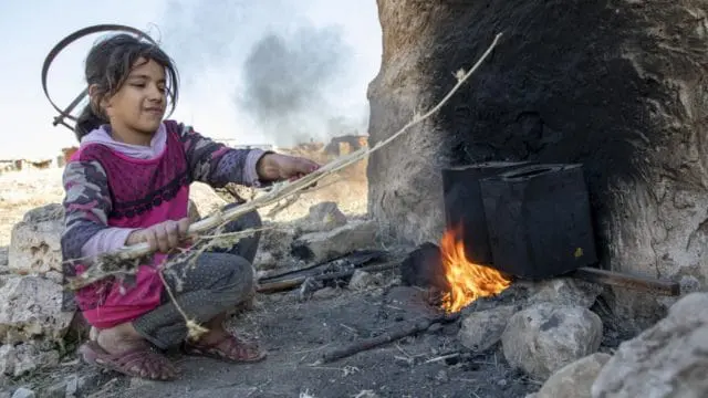 A girl heats water over fire.